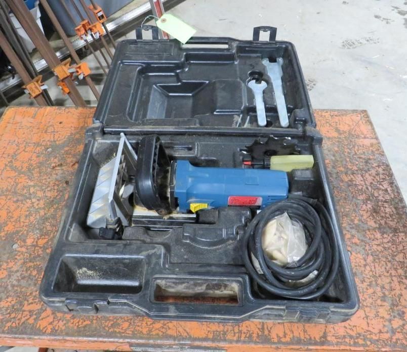 Black tool case open with a blue and black router, accessories, and power cord on an orange tabletop.