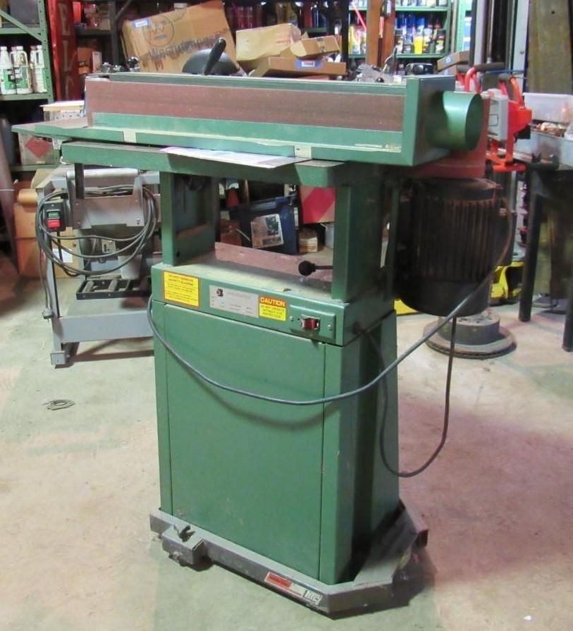 Green industrial belt sander in a workshop.