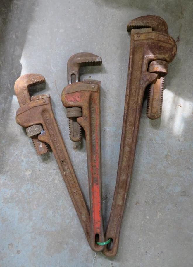 Three pipe wrenches on a gray surface, ranging in size and held together by a green band.
