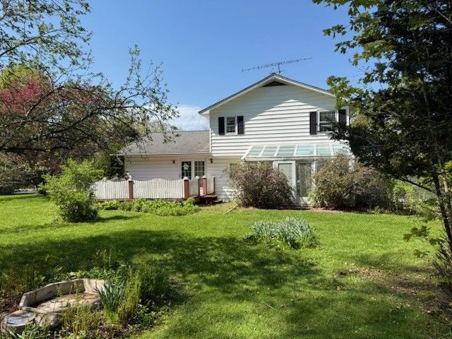 White two-story house with a small glassed-in porch and antenna on the roof, viewed from a green lawn on a sunny day.