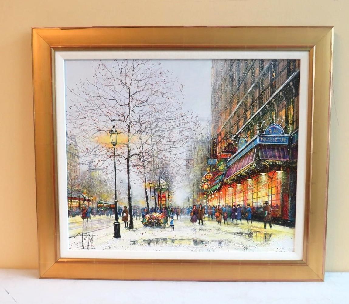 Oil painting of a European street scene at dusk, framed in gold. Buildings, lights, people, and a tree are depicted.