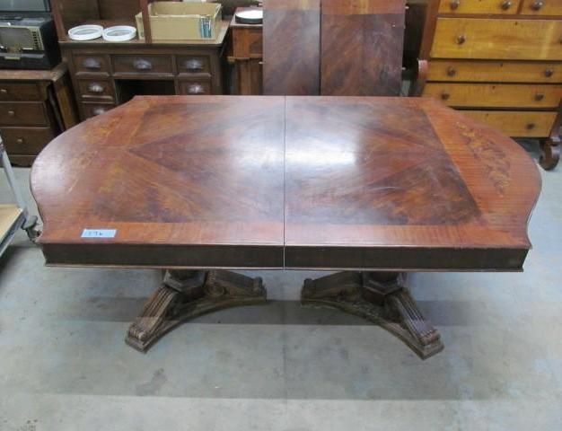 Brown wooden dining table with ornate pedestal bases in a room with other furniture.