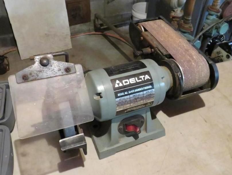 Delta belt sander with clear plastic guard on a concrete floor.