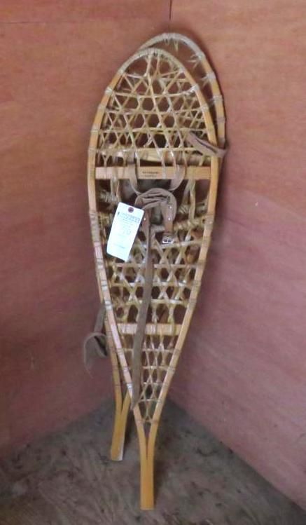 Pair of wooden snowshoes leaning against a wooden wall; tan leather straps.