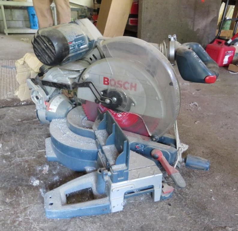 Blue Bosch miter saw, dusty, on a concrete floor.