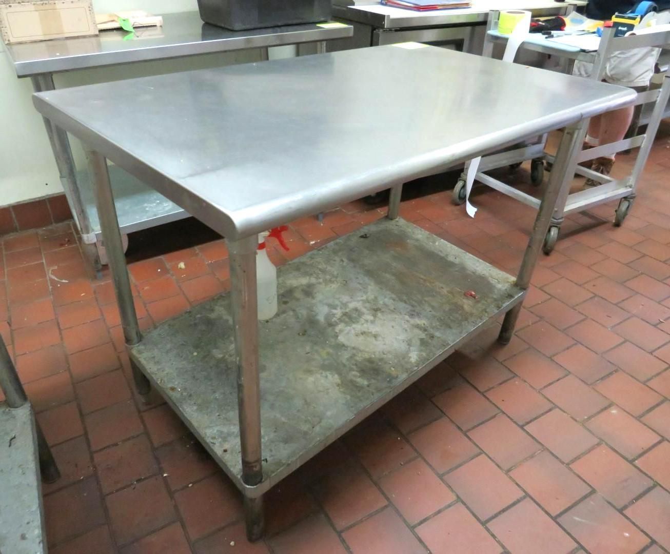 Stainless steel prep table with a lower shelf in a commercial kitchen setting.