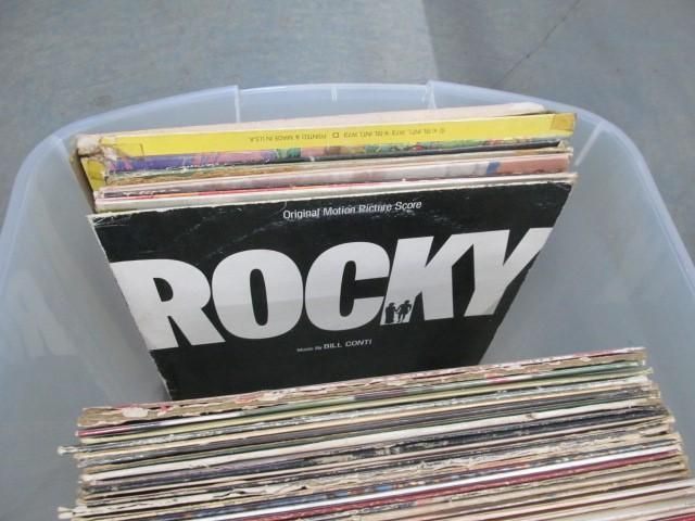 Stack of vinyl records in a plastic bin; Rocky soundtrack album cover visible.