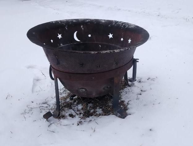 Metal fire pit with moon and star cutouts on snow.