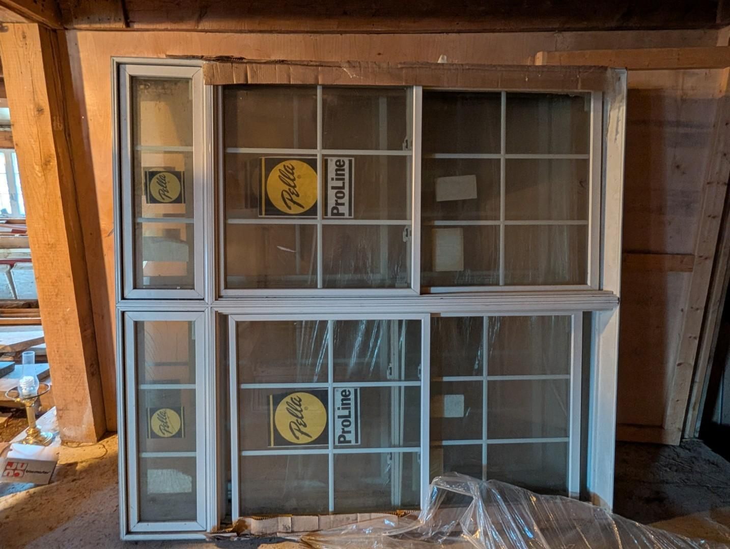Three white-framed windows stacked in a wooden garage, with yellow stickers on the glass.