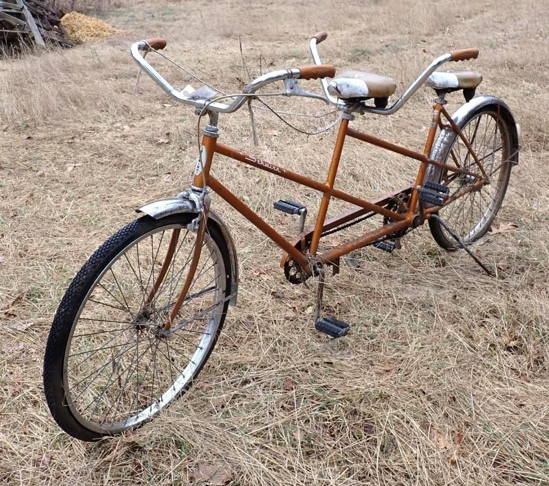 An orange vintage tandem bicycle parked on a patch of grass.