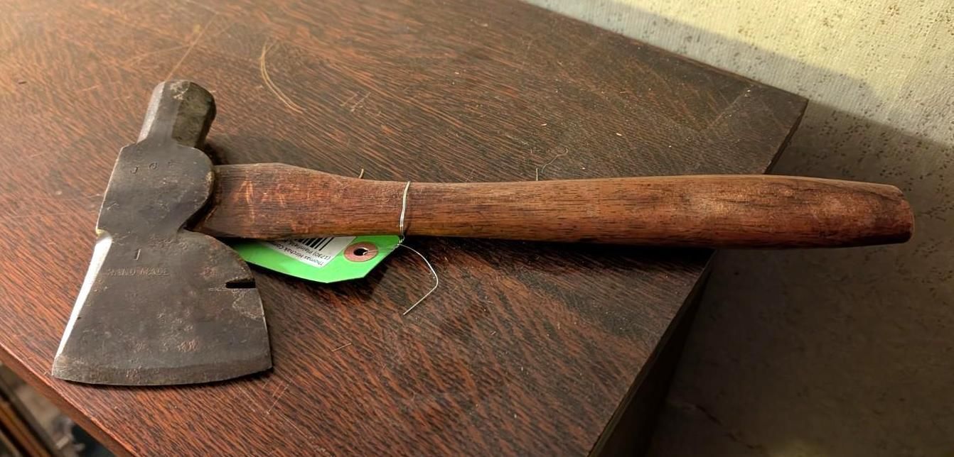 A vintage hatchet with a metal head and wooden handle lies horizontally on a dark wood surface.