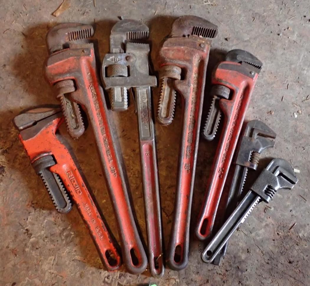 A collection of seven pipe wrenches and adjustable wrenches of varying sizes arranged in a fan shape on a concrete floor.