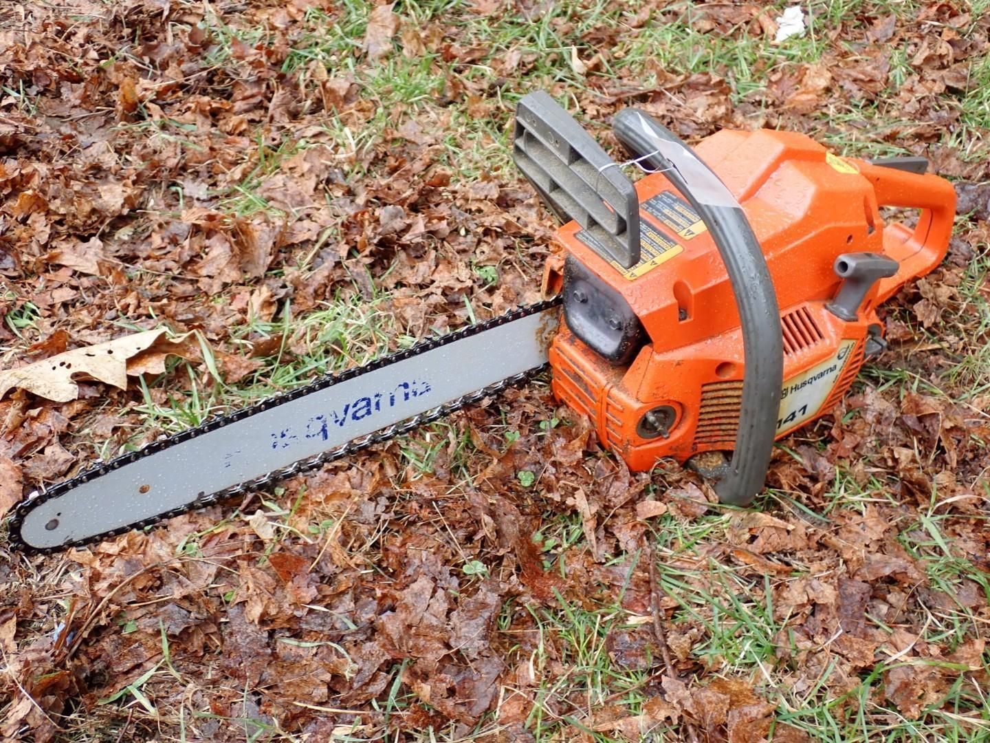An orange Husqvarna chainsaw rests on a patch of grass.