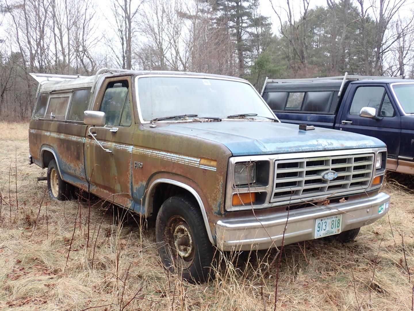 A blue and brown Ford pickup truck with a camper shell parked in a field.