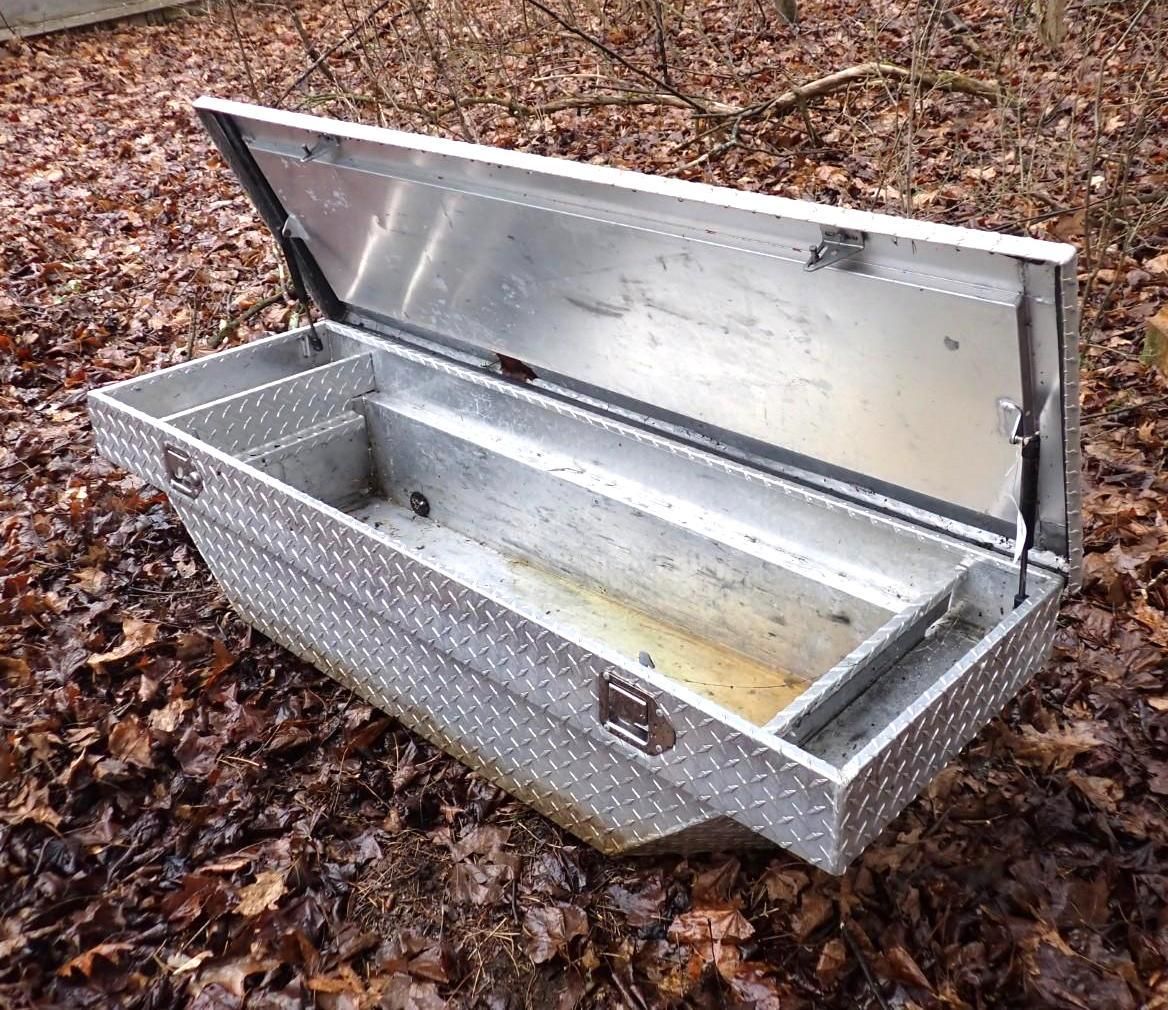 An open, diamond-plate aluminum truck tool box.