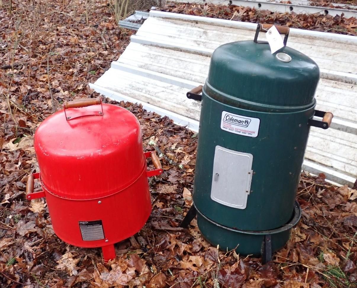 A red and a green portable smoker grill standing outdoors.