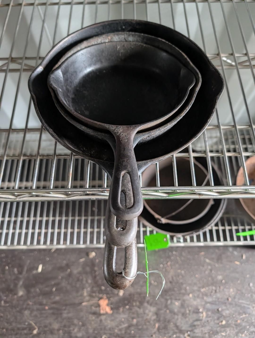 A stack of three nested black cast iron skillets with oval-hole handles sitting on a metal wire shelf.