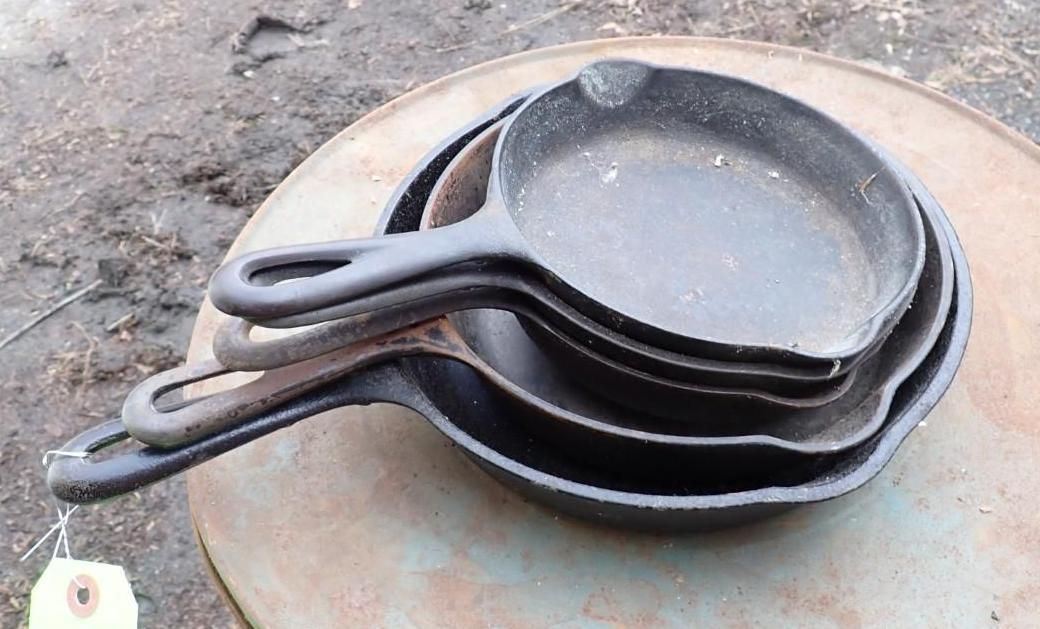 A stack of three nested black cast-iron skillets with handle holes, resting on a flat, circular metal surface.
