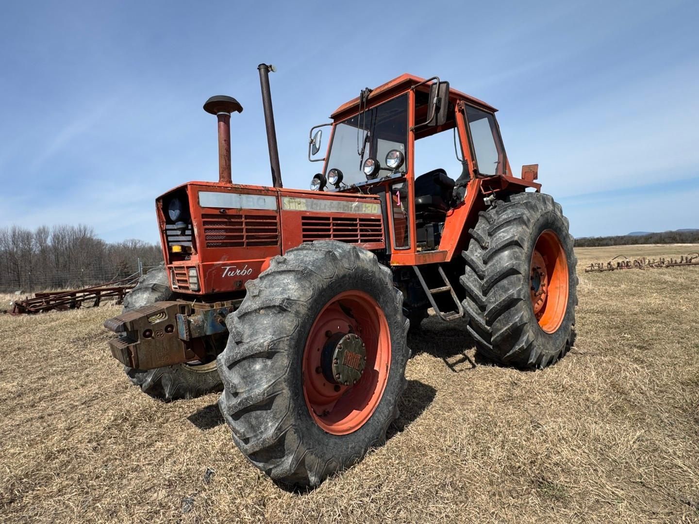 A large, orange Fiat tractor with a cab, parked on a grassy field under a clear blue sky.