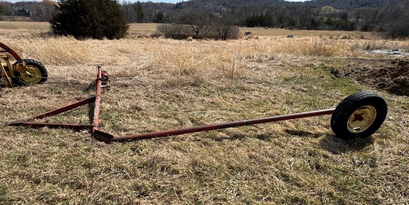 A red, V-shaped steel frame with a single wheel attached to the end, lying on a grass field under a blue sky.