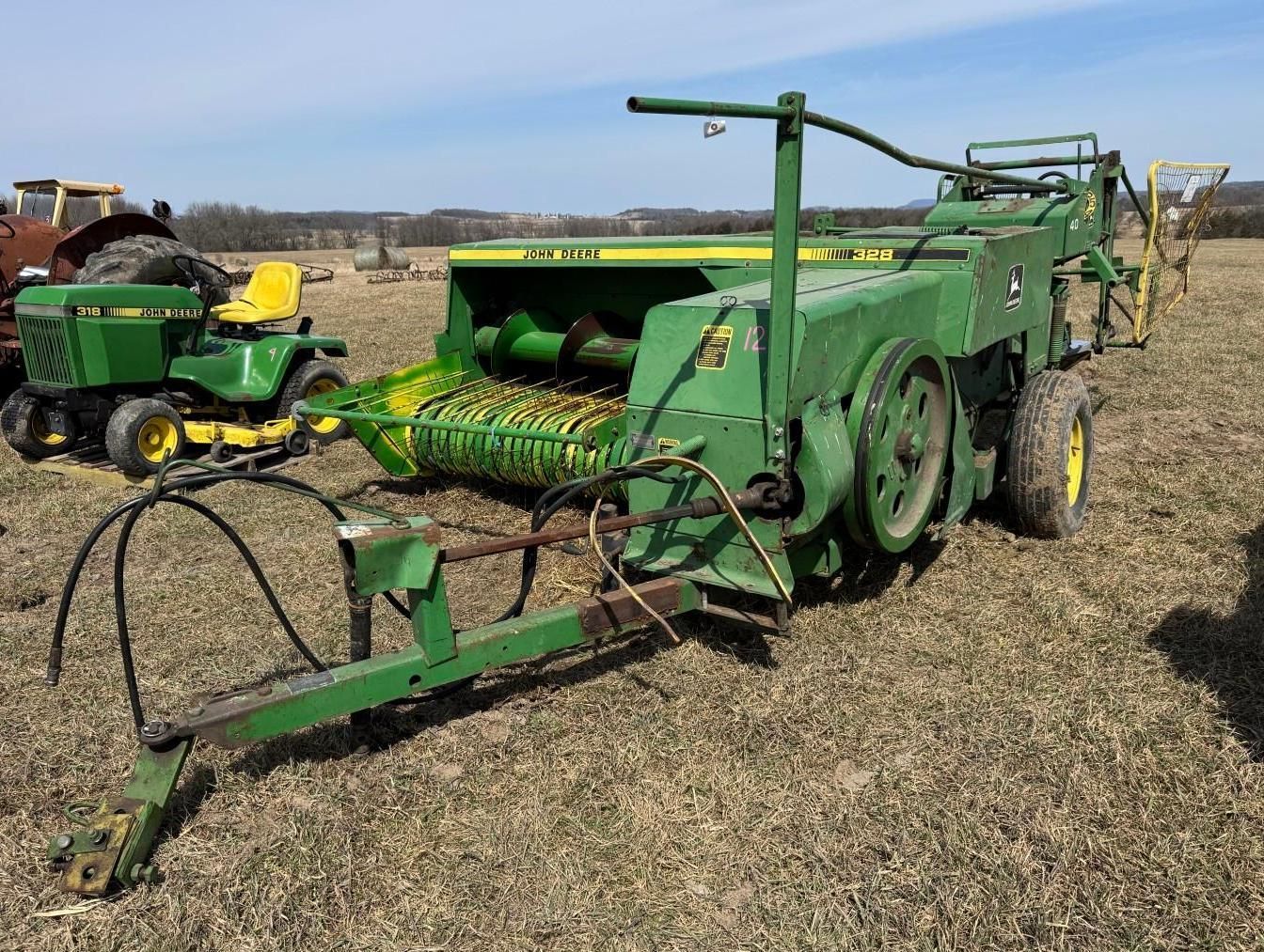 A green John Deere square baler sits in a field.