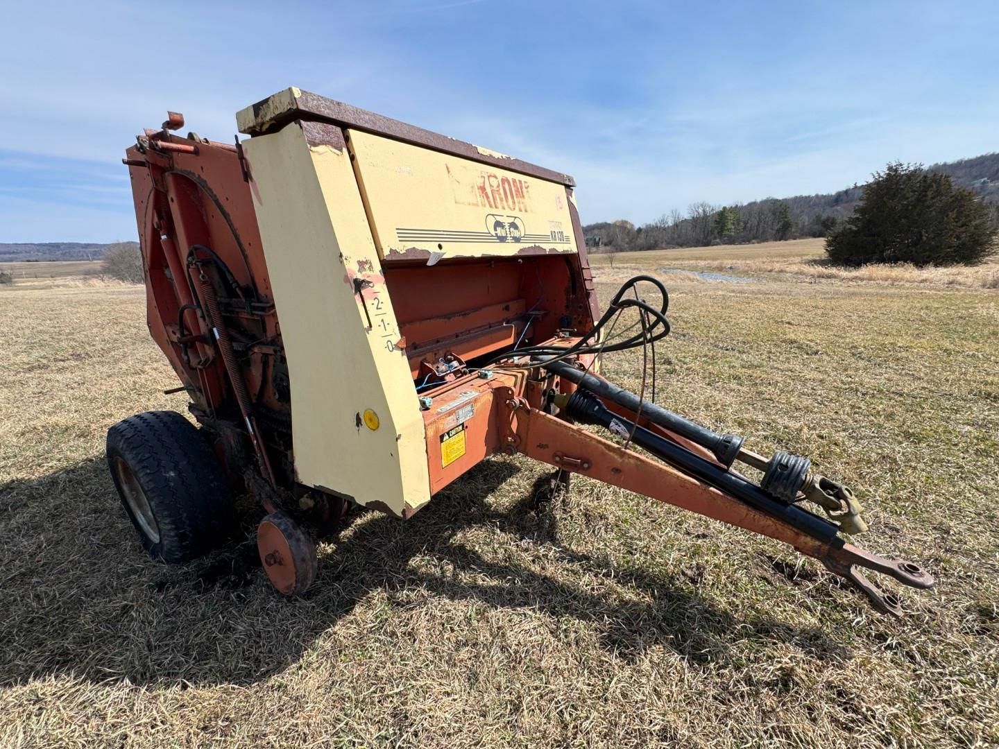 An orange and cream-colored Vermeer round baler sits in an open field under a blue sky.