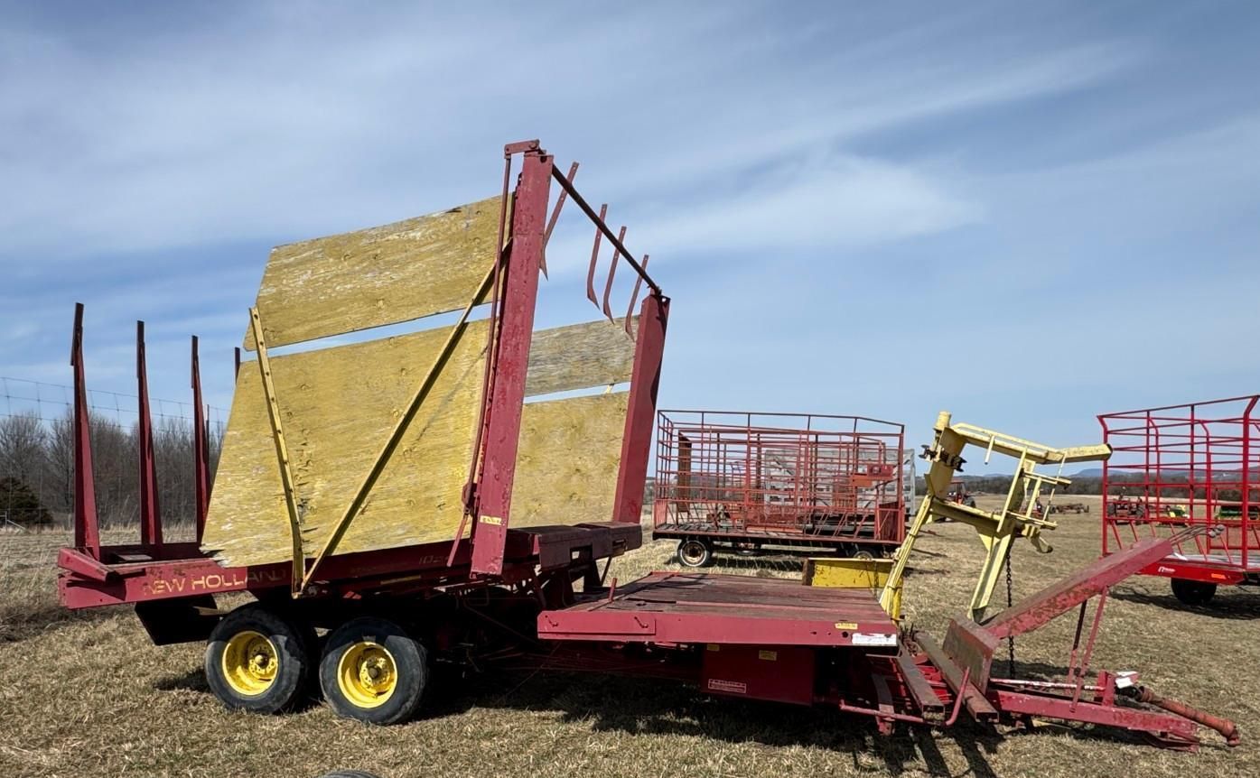 A red agricultural trailer with a wooden partition stands in a field under a clear blue sky.