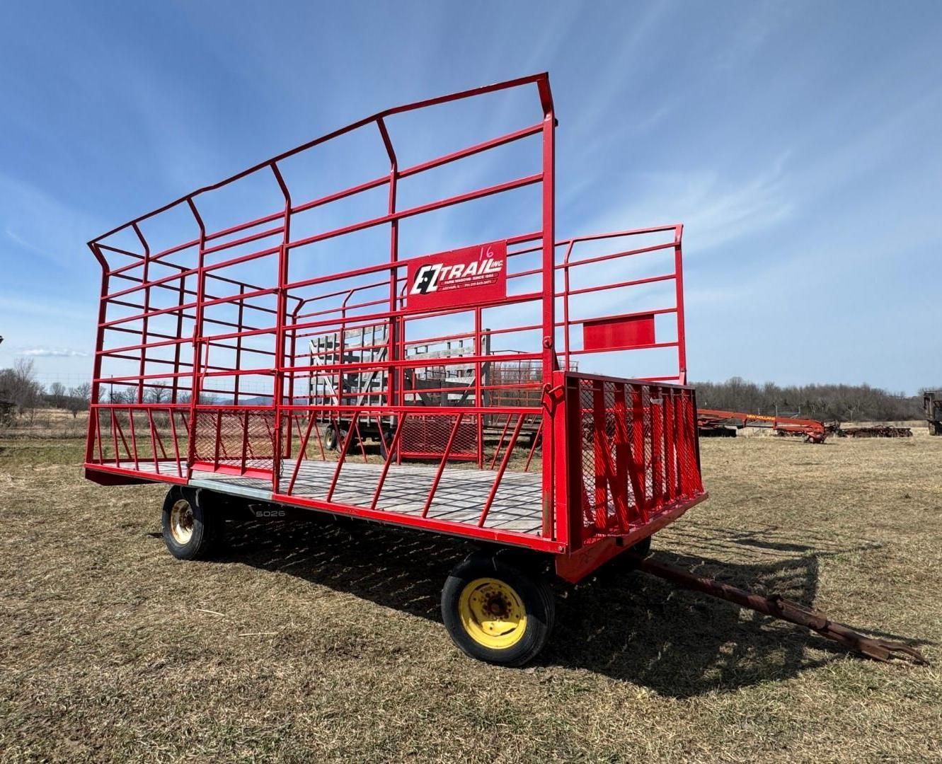 A red EZ-Trail forage wagon with a wire cage frame sits in a field under a blue sky.