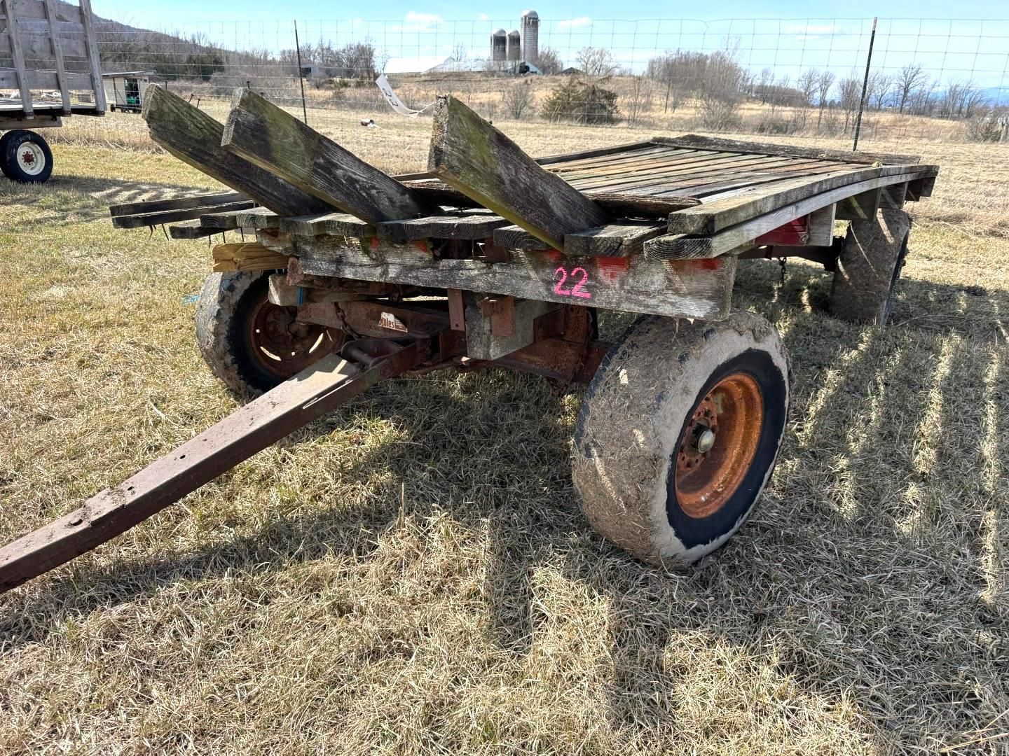 A farm wagon with wooden beams and orange wheels sits in a field on a sunny day.