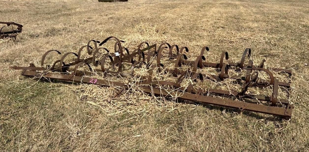 An antique metal farm harrow with curved teeth sits resting on a grassy field.