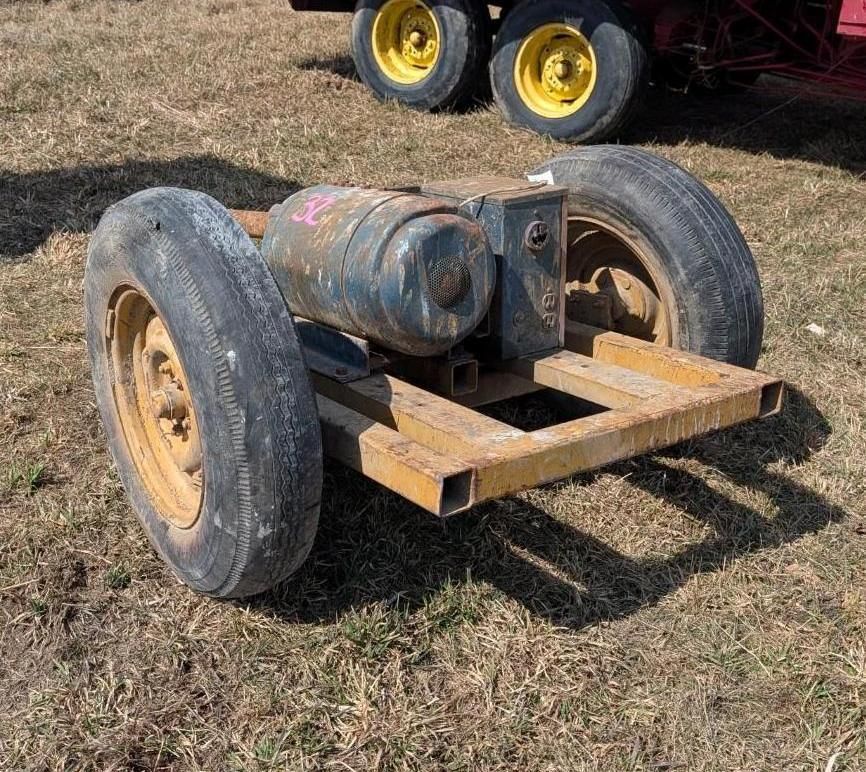 A portable industrial air compressor mounted on a yellow metal frame with two black tires, sitting on grass.