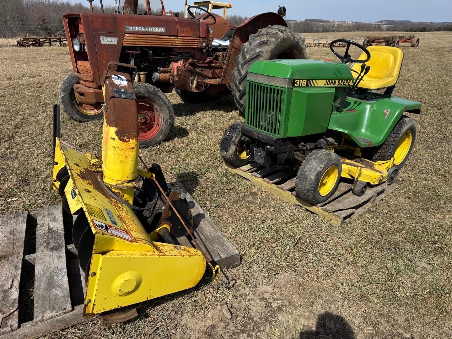 A green John Deere lawn tractor, a yellow snow blower attachment on a pallet.