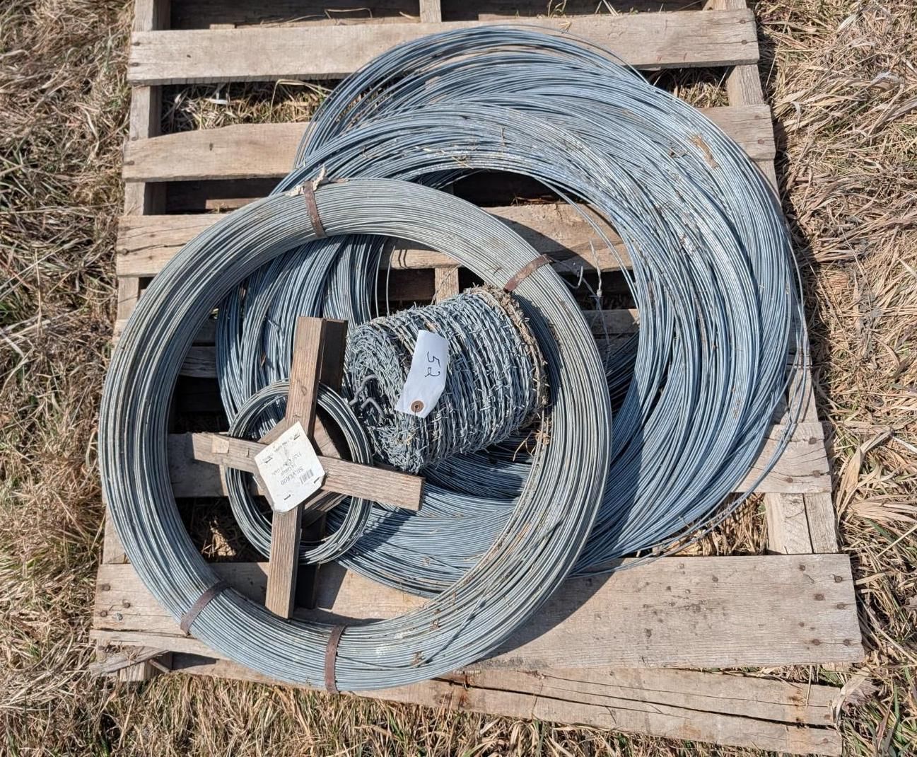 Multiple coils of silver, textured barbed wire rest on a wooden pallet outdoors.