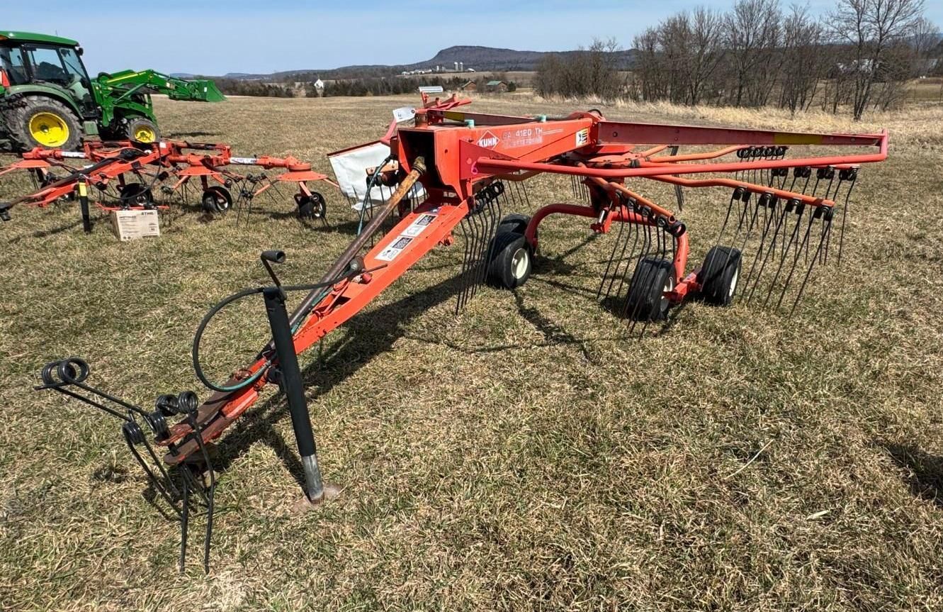 An orange rotary hay rake sits in a grassy field.
