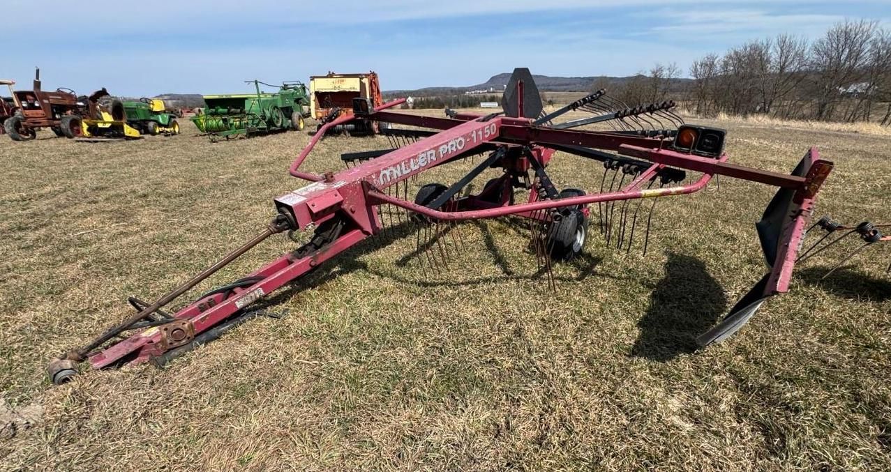 A red rotary hay rake sits on a grassy field.