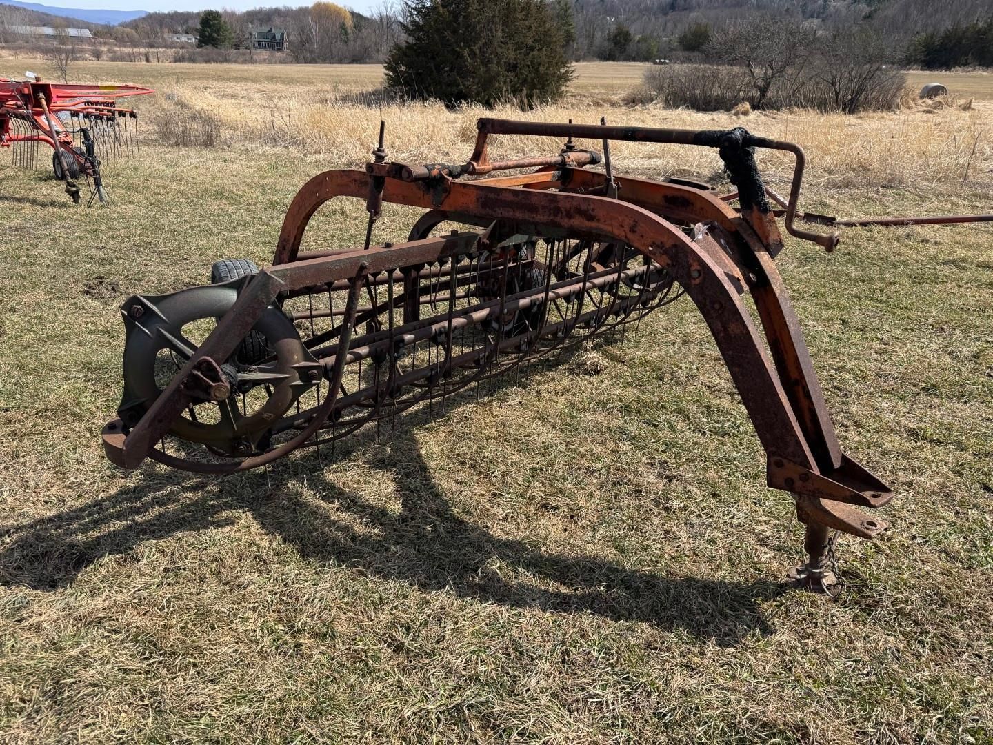 A vintage horse-drawn hay rake sits in a grassy field on a sunny day.