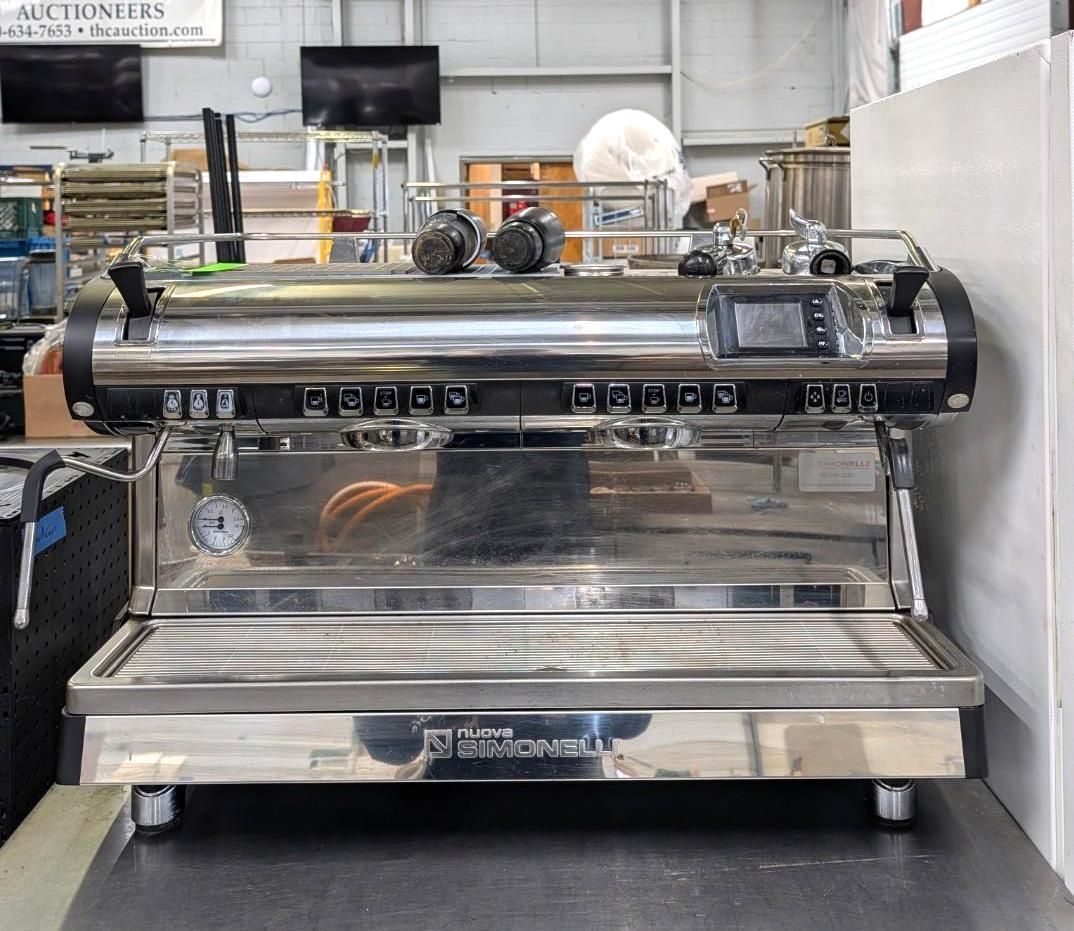 Large stainless steel commercial espresso machine on a counter in a workshop or cafe equipment showroom
