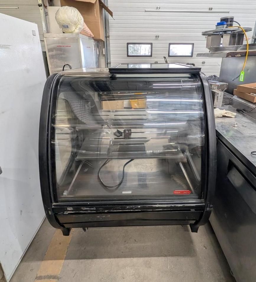 Glass-front countertop display case in a workshop, with shelves and a reflective black frame.