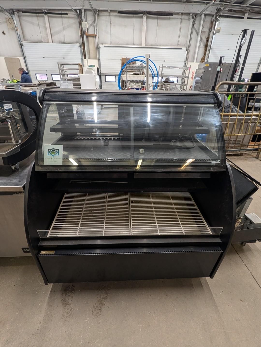 Black refrigerated deli display case with glass front in a warehouse or workshop setting