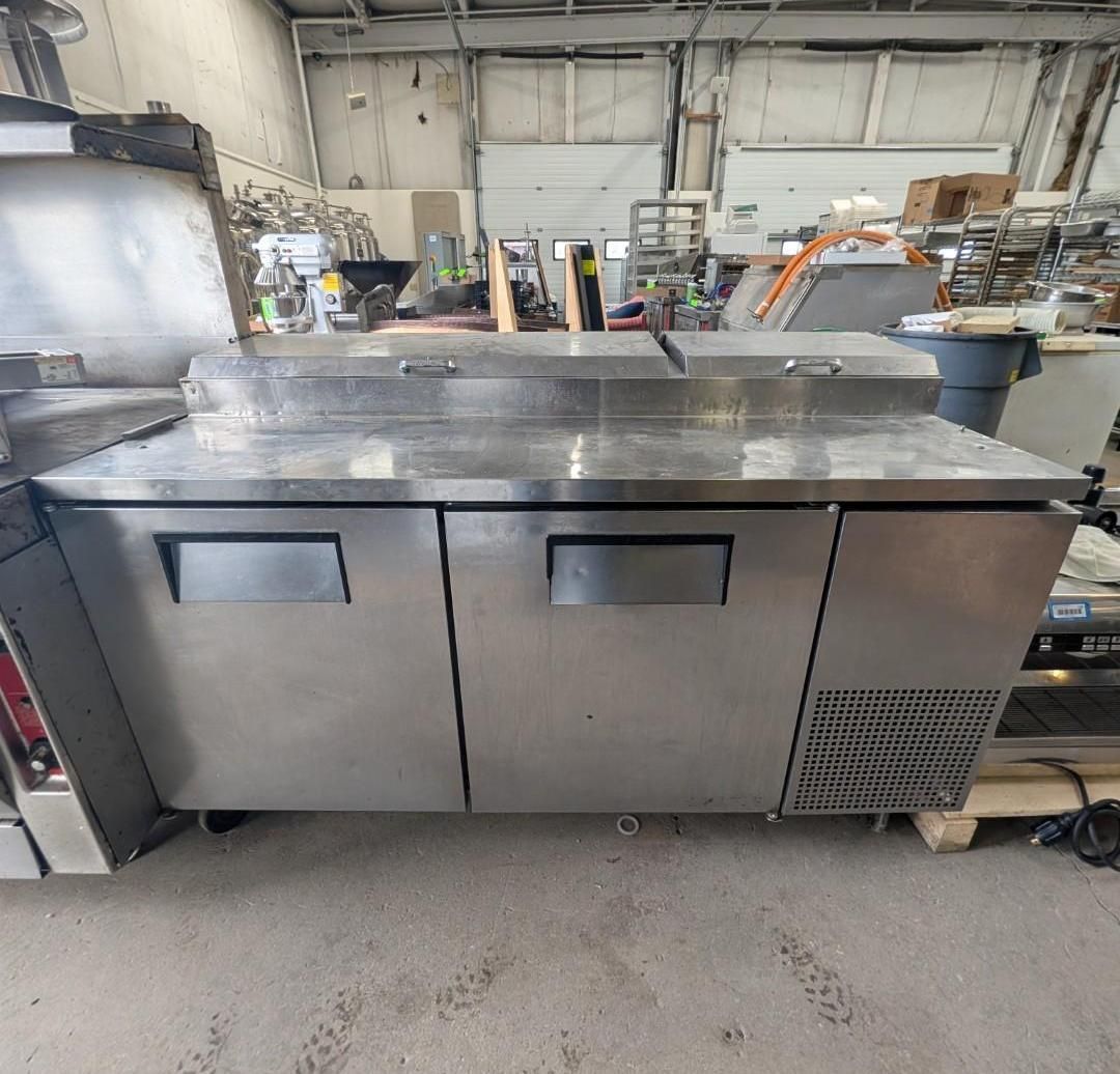 Stainless steel industrial prep table with two cabinet doors and a vented side panel in a workshop.