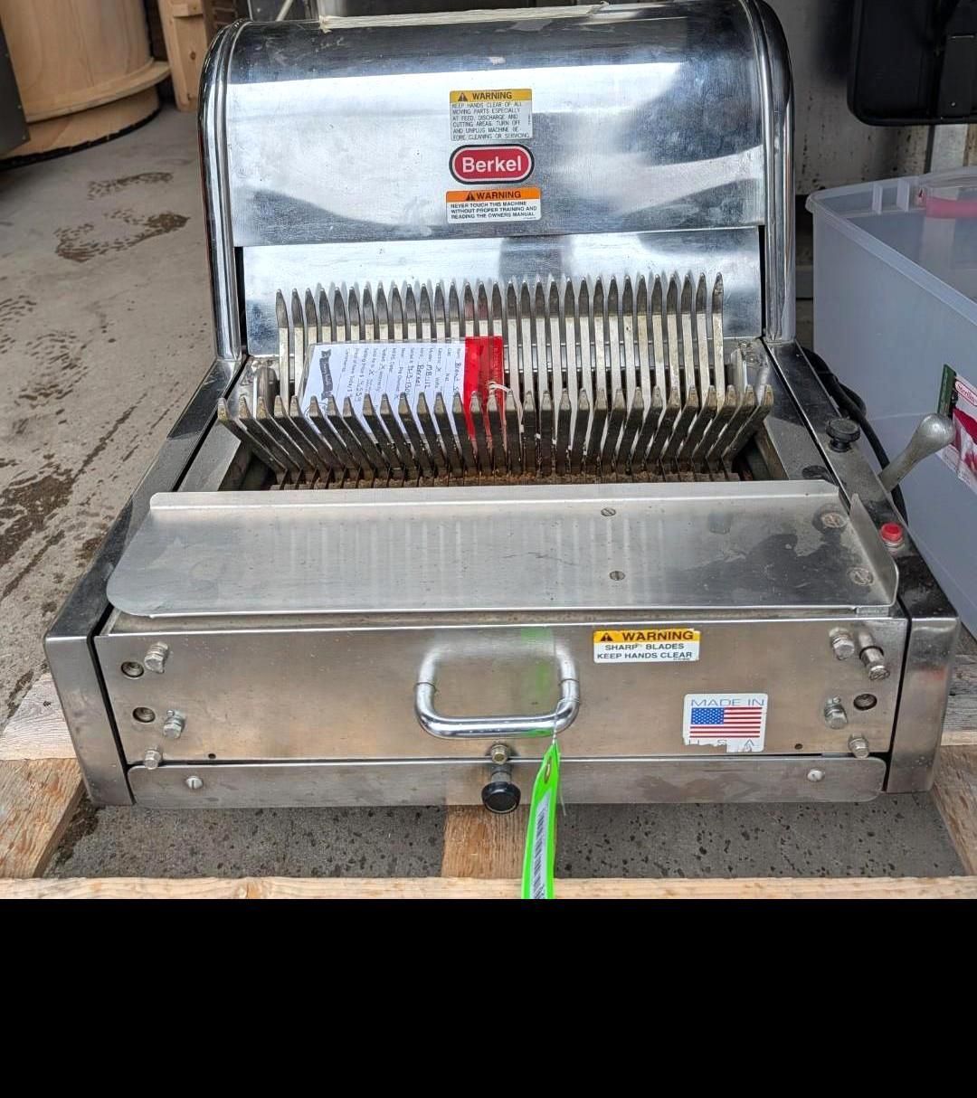 Stainless steel commercial meat slicer on a floor, with a red handle and blade guard open.