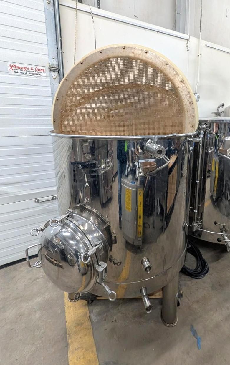 Stainless steel industrial tank with a domed top in a warehouse setting