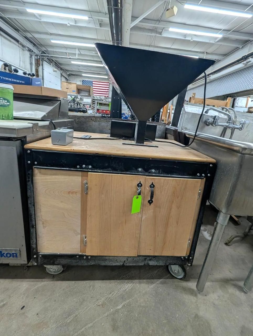 Wood cabinet cart with a black funnel hopper in a workshop or warehouse.