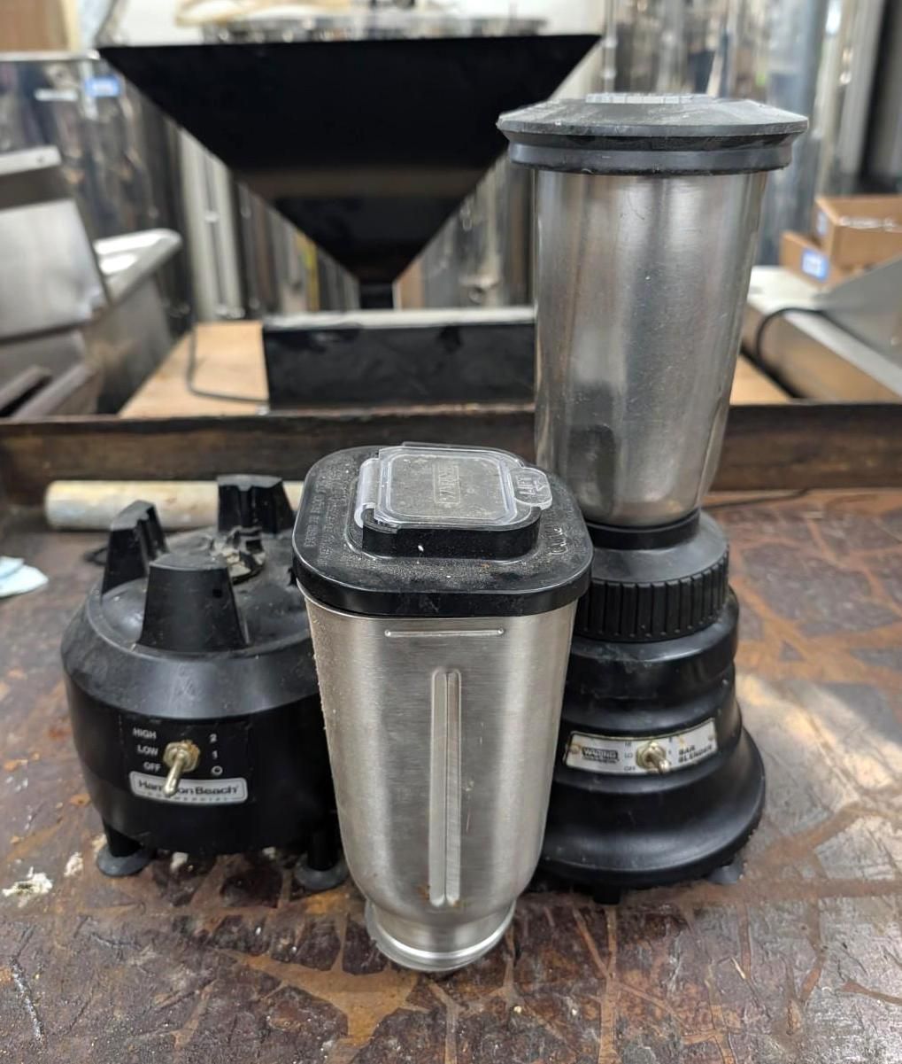 Three metal blender jars and bases on a countertop in a kitchen or workshop.