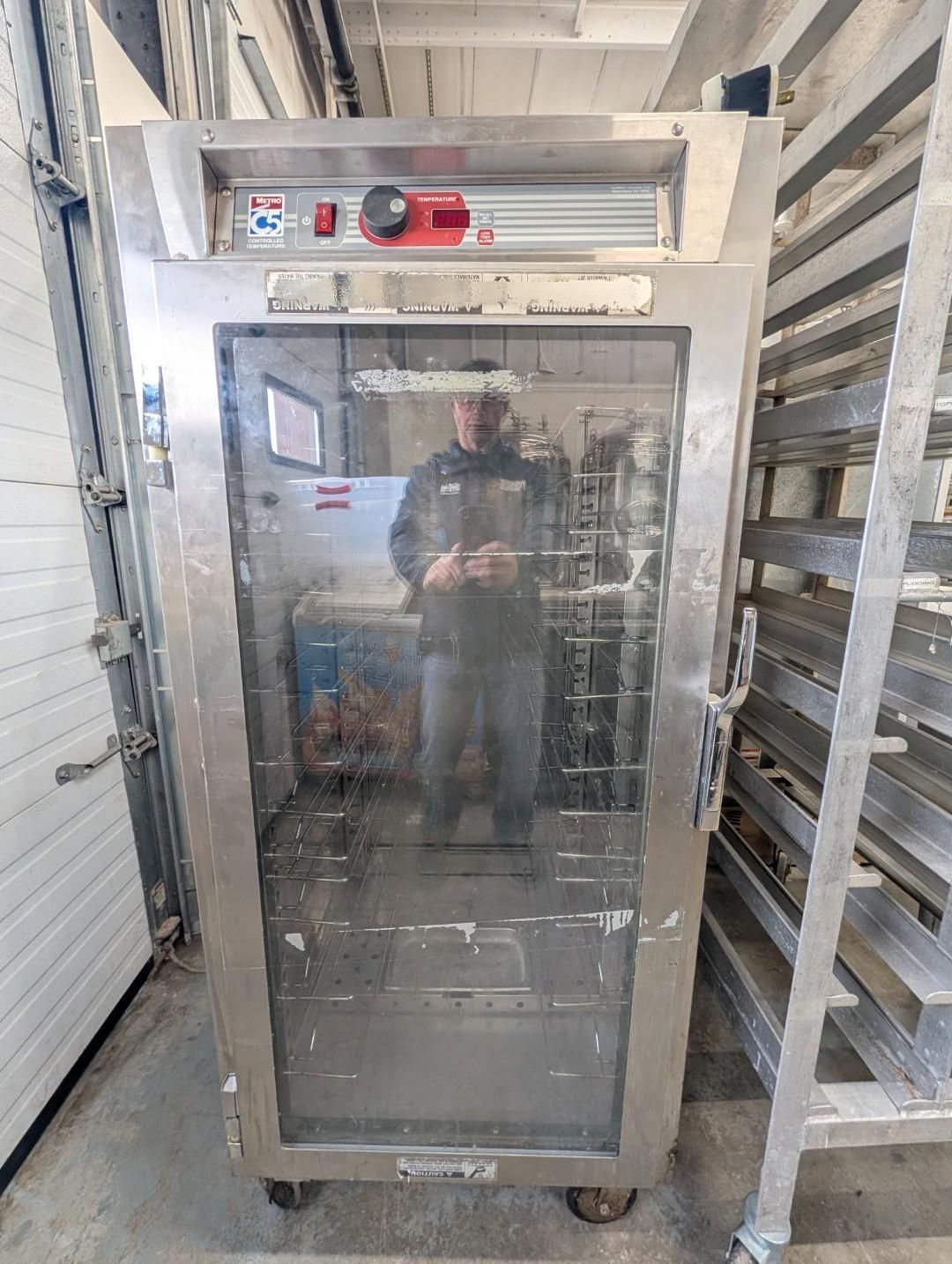 Large stainless steel commercial oven with glass door in a bakery or kitchen storage area.
