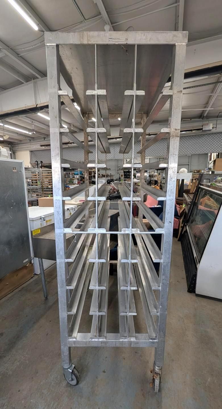 Tall metal cart on wheels in a workshop, with shelves and hanging hooks, viewed from the front.