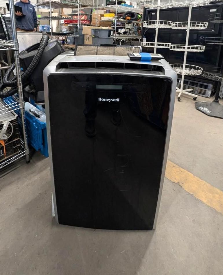 Black Honeywell portable air conditioner in a warehouse aisle, with shelves and equipment in the background.