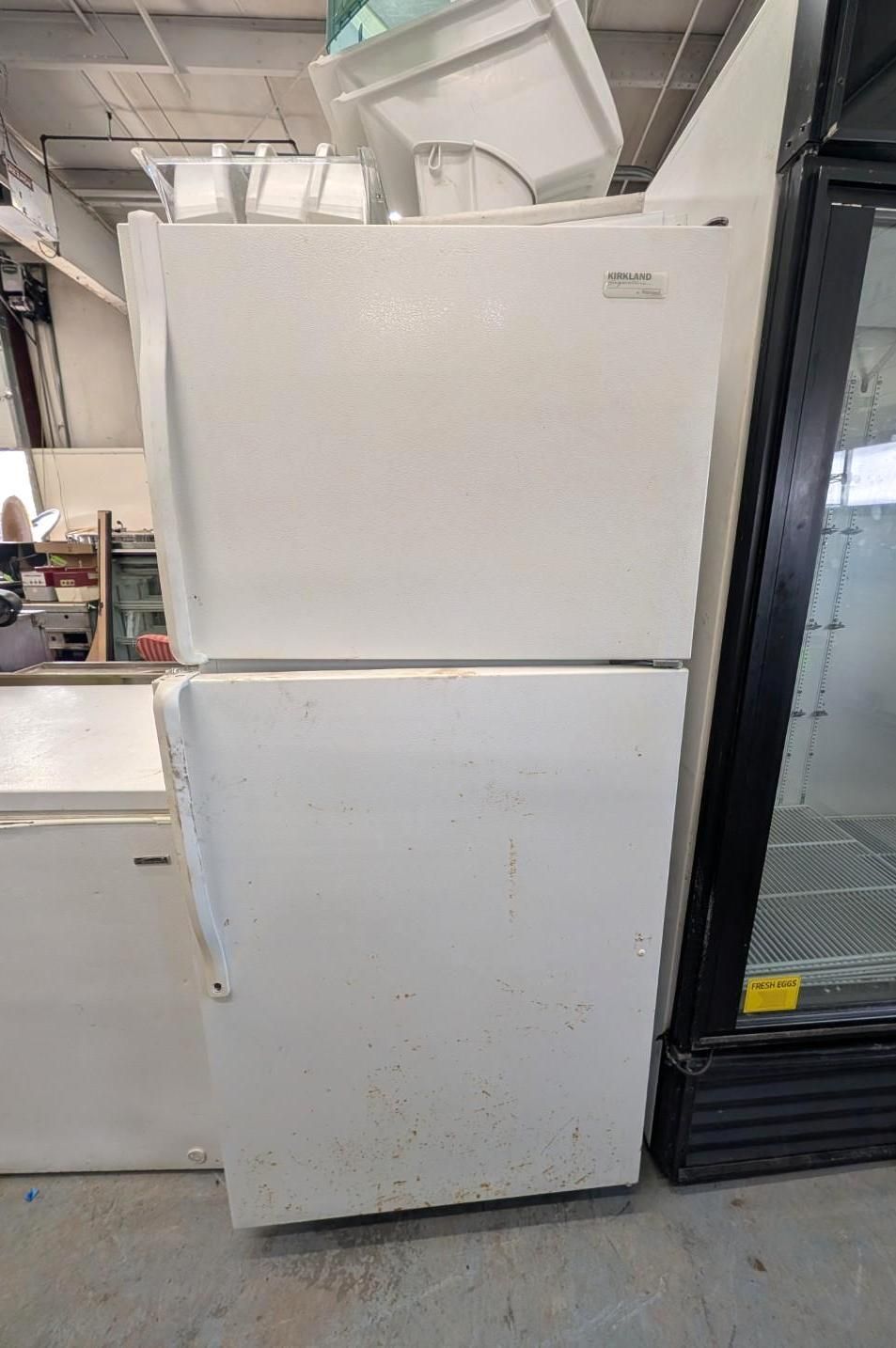 Two stacked white refrigerators in a storage area