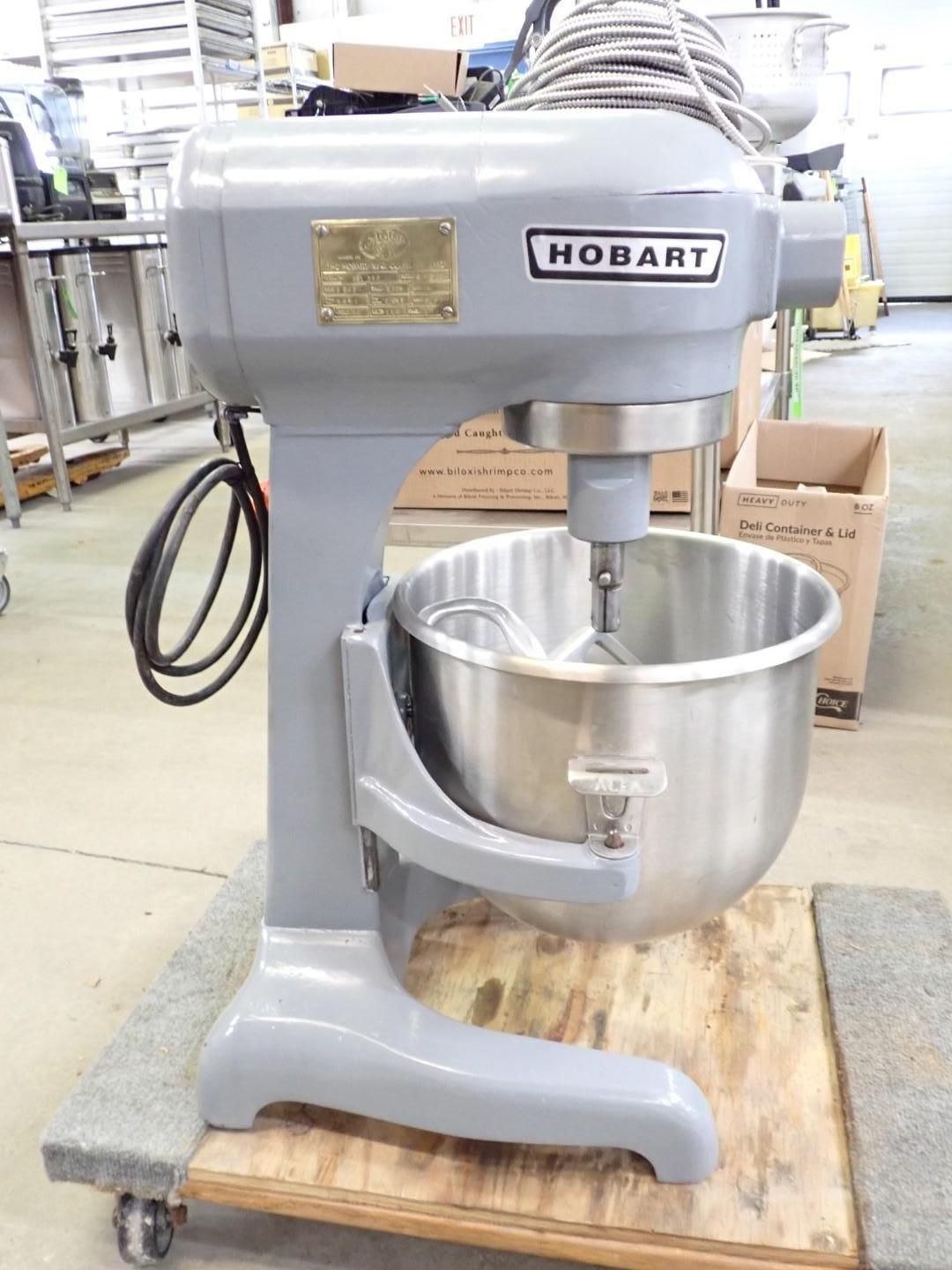 Gray Hobart commercial stand mixer with stainless steel bowl on a wooden pallet in a warehouse