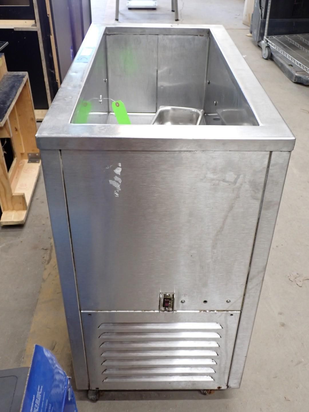 Stainless steel commercial sink with front vented panel in a warehouse-like setting